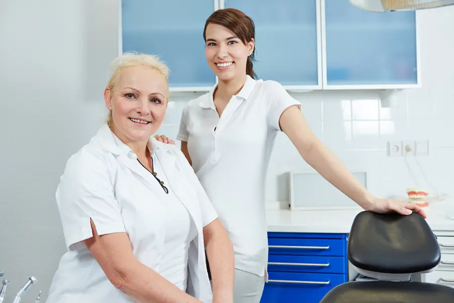 Two friendly dental professionals standing confidently in a clean, modern clinic, ready to provide expert care. This image highlights a skilled and trustworthy team dedicated to patient comfort and high-quality dental treatments in a welcoming environment.