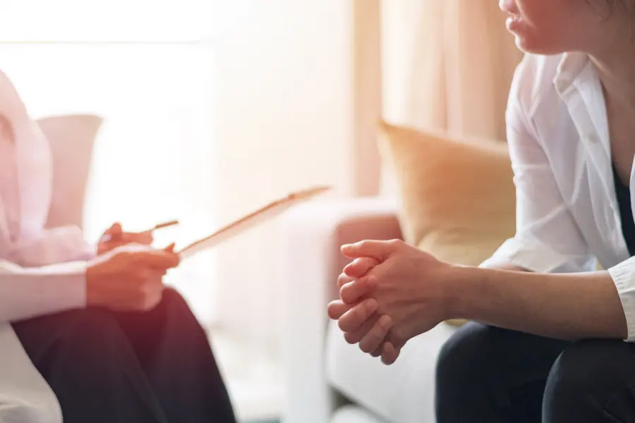 A calm, inviting therapy session in a warm and comfortable setting. The client, holds their hands together, listening attentively as the therapist engages in a compassionate conversation, creating a safe space for healing and emotional support, fostering trust and connection.